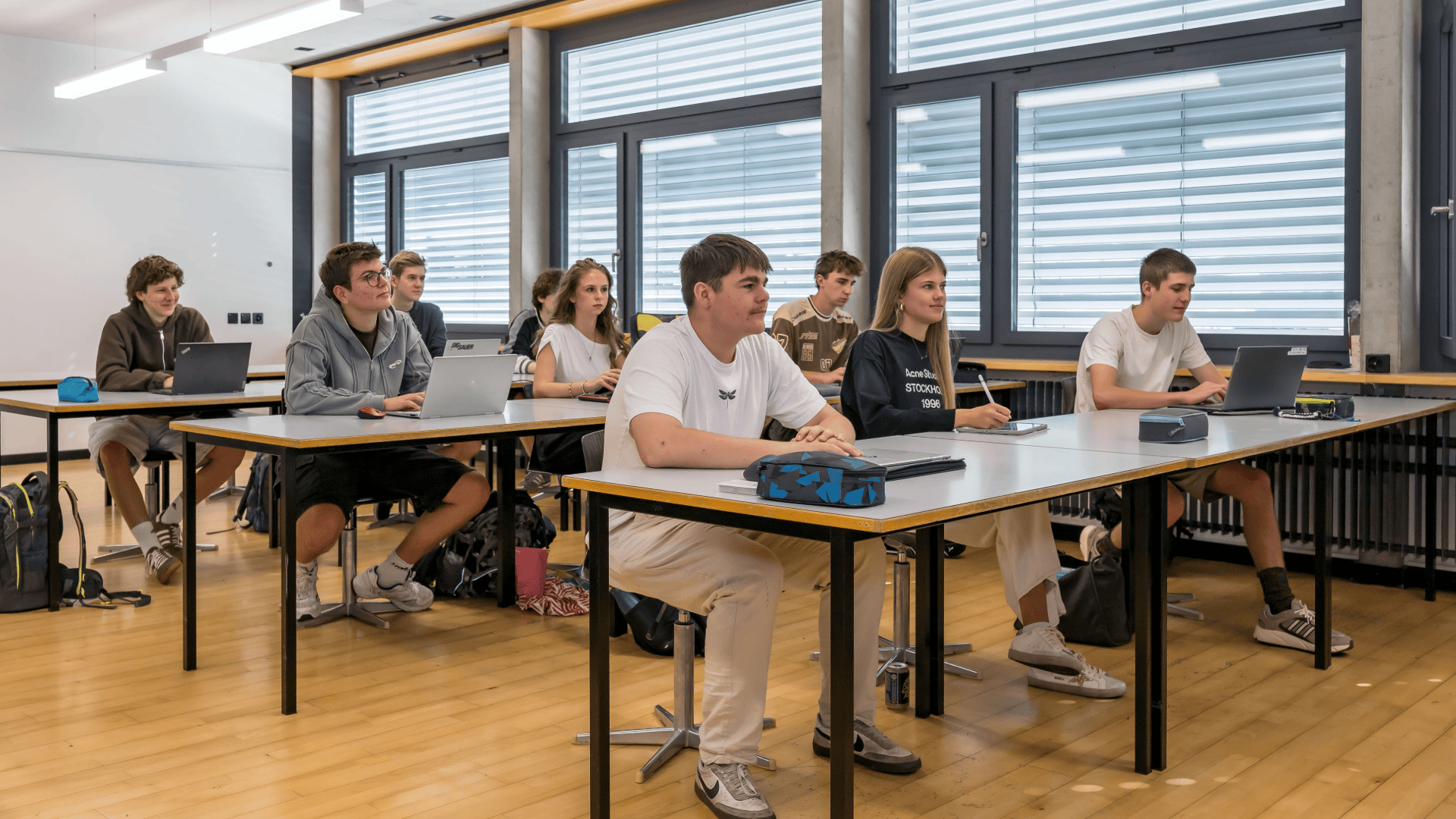 Die Schüler sitzen an ihren Schreibtischen im Klassenzimmer, arbeiten an ihren Laptops und machen sich Notizen.