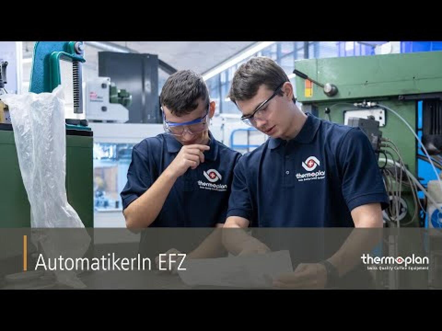 Zwei Personen in marineblauen Thermoplan-Shirts und Schutzbrillen arbeiten gemeinsam in einer Fabrik und lesen Unterlagen. Der Text lautet „AutomatikerIn EFZ“, und in der rechten unteren Ecke ist das Thermoplan-Logo zu sehen.
