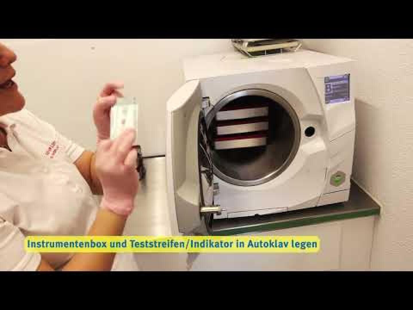 Eine Person, die Handschuhe trägt, legt einen Instrumentenkasten und einen Teststreifen in einen offenen Autoklav.