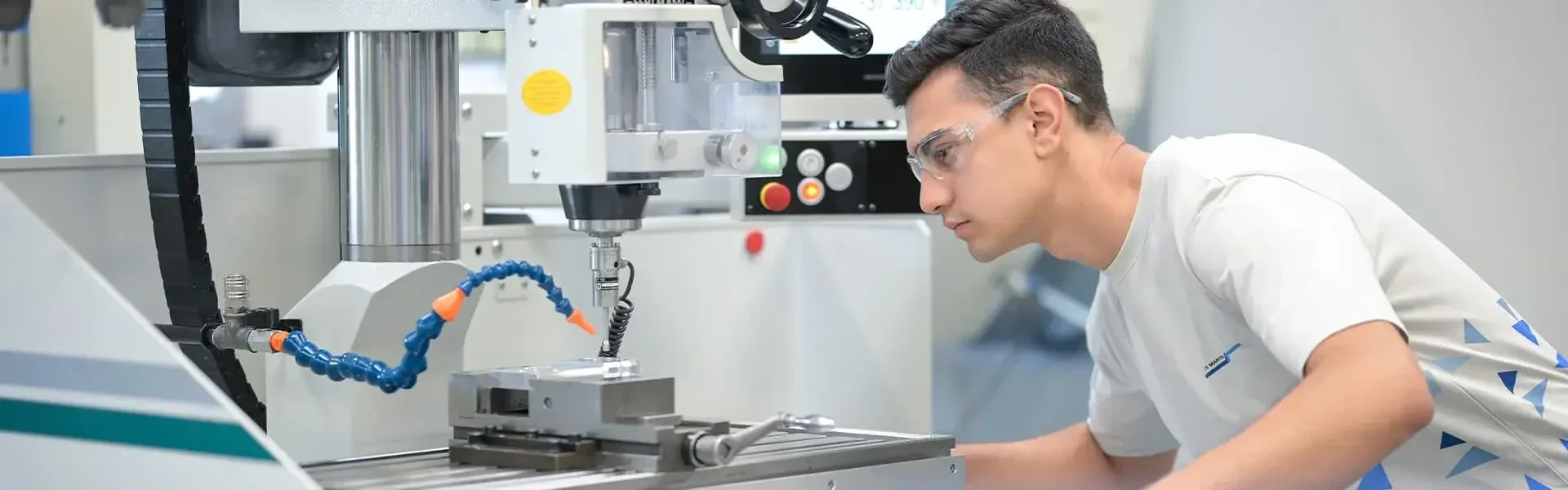 Ein Techniker mit Schutzbrille überwacht eine CNC-Fräsmaschine beim Bearbeiten eines Metallwerkstücks.