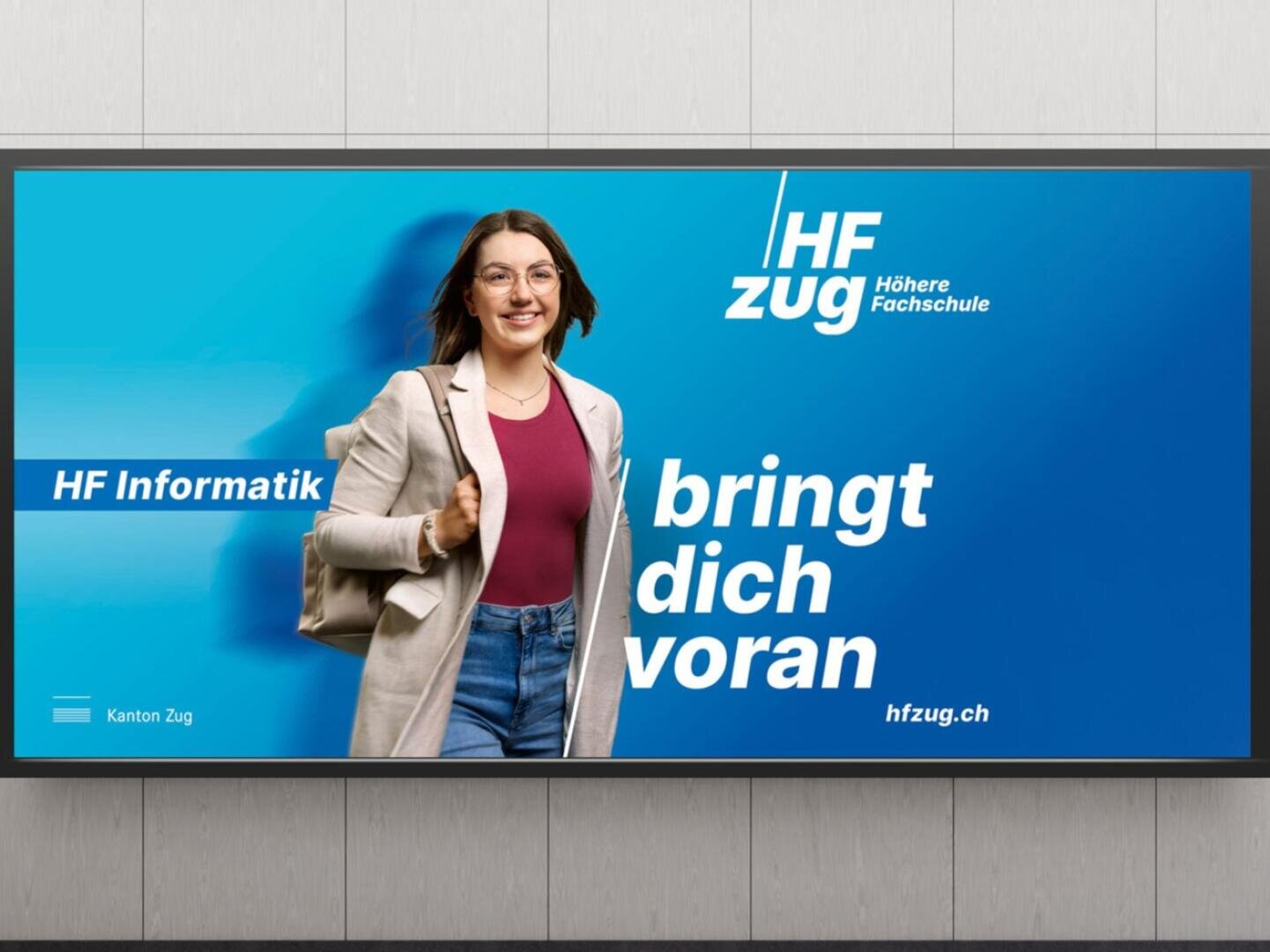 Eine lächelnde junge Frau mit Brille, die einen beigen Mantel trägt und eine Tasche mit sich führt, geht selbstbewusst vor einem blauen Hintergrund mit dem Text "HF Informatik bringt dich voran" und "HF Zug Höhere Fachschule.".