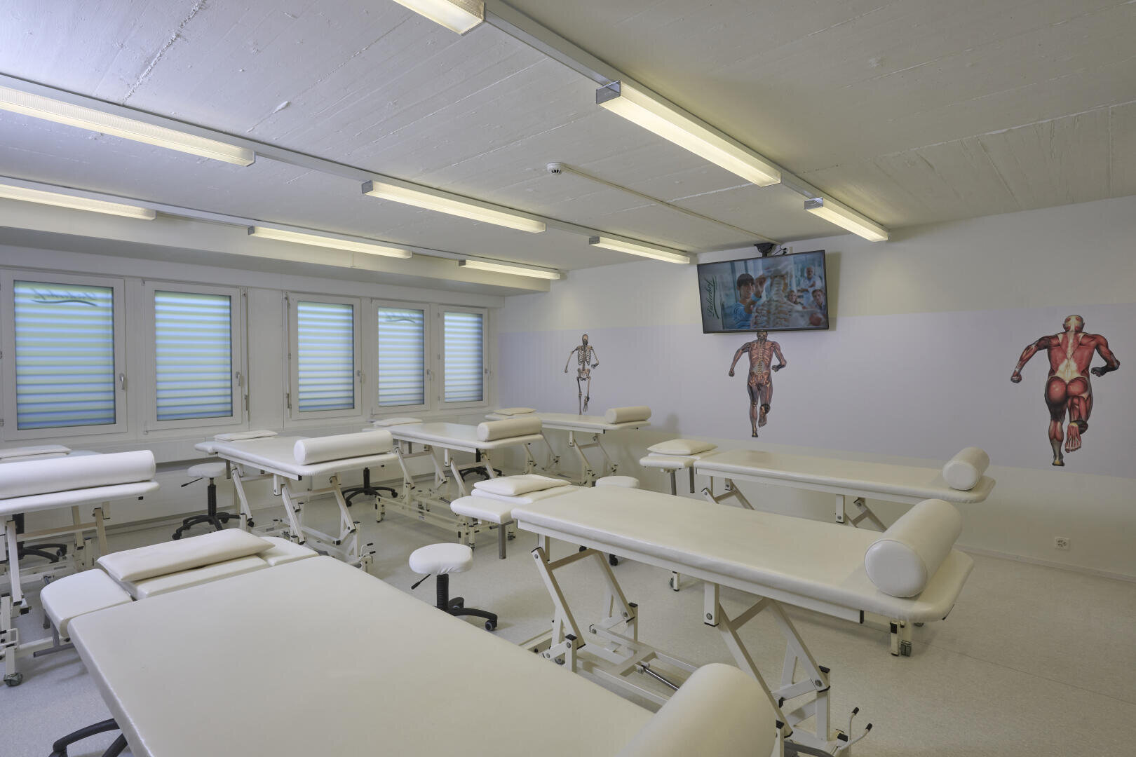 Ein Zimmer mit weißen Betten und einem Fernseher an der Wand.