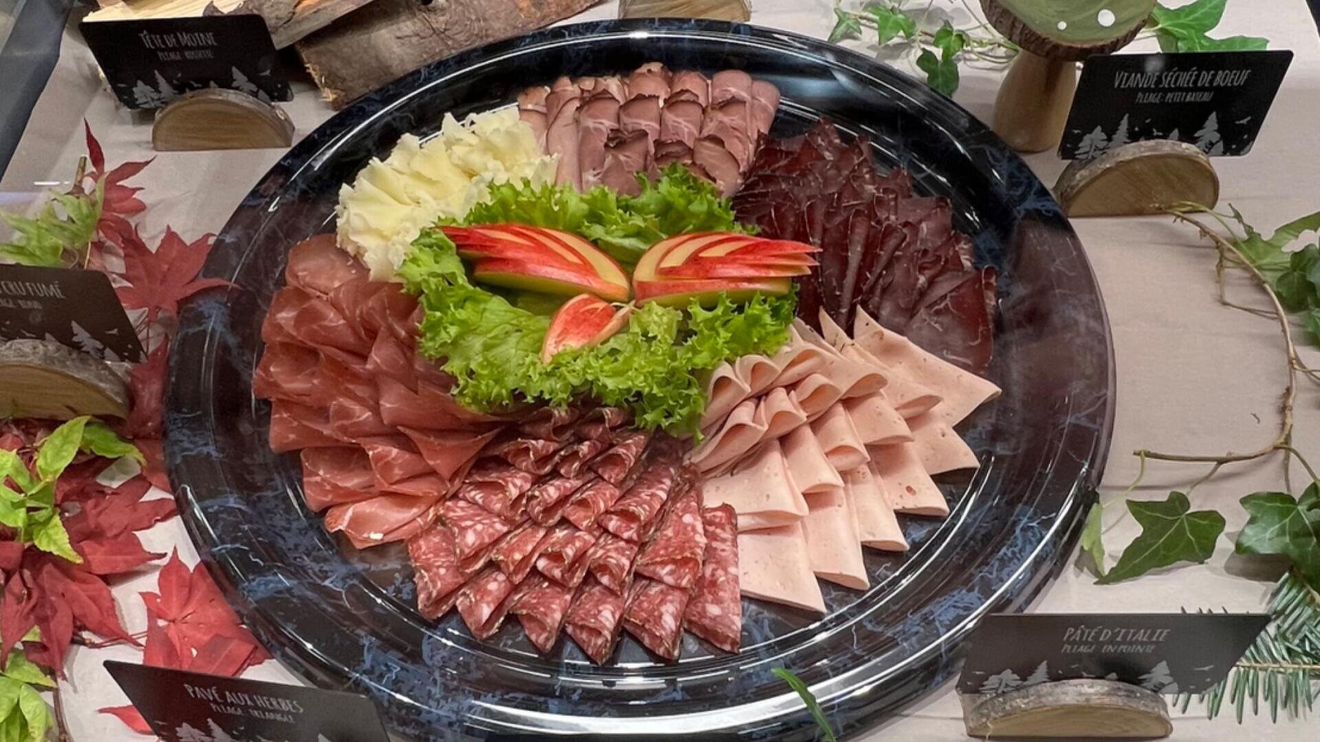 Eine Platte mit verschiedenen Aufschnitt- und Käsesorten, garniert mit Salatblättern und Apfelscheiben, kreisförmig auf einem schwarzen Tablett angerichtet.