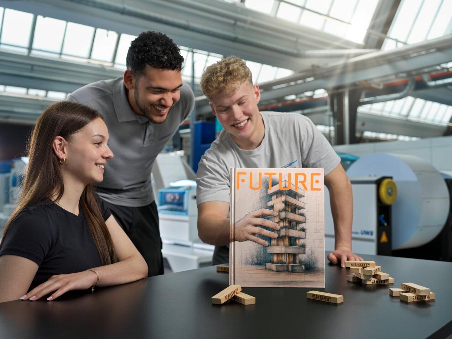 Zwei junge Männer und eine Frau lächeln, während sie ein Buch mit dem Titel Future betrachten, auf dessen Cover eine Hand abgebildet ist, die einen Turm baut.