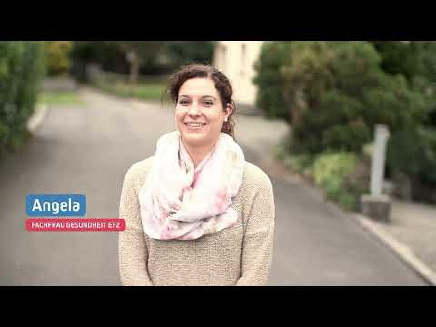 Eine Frau mit lockigem braunem Haar, die einen hellen Schal und einen beigen Pullover trägt, steht draußen auf einem Weg. Auf dem Bild ist der Text „Angela“ und „Fachfrau Gesundheit EFZ“ zu lesen. Im Hintergrund sind Bäume und ein Gebäude zu sehen.