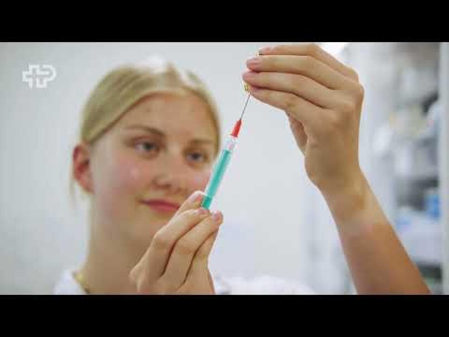 Eine Mitarbeiterin des Gesundheitswesens mit blondem Haar hält eine Spritze in der Hand und zieht vorsichtig eine Flüssigkeit aus einem Fläschchen in einer klinischen Umgebung auf.