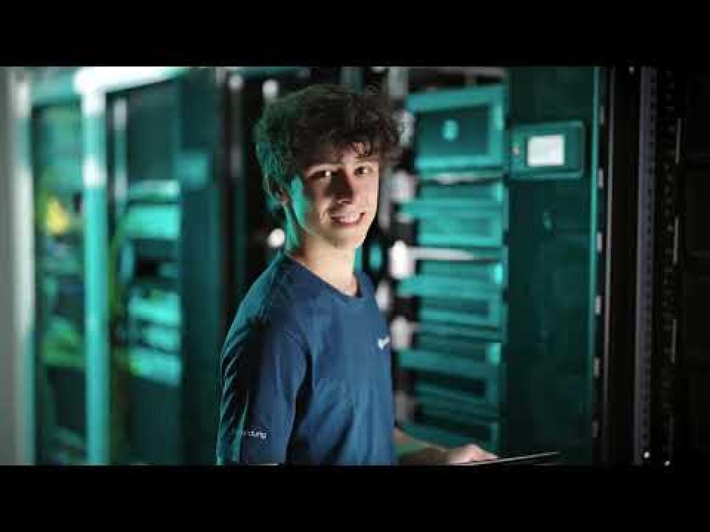Ein junger Mann in einem blauen T-Shirt, der in einem Serverraum steht.