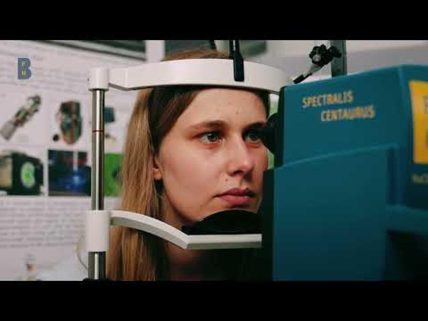 Eine Frau sitzt mit dem Kinn auf einer Stütze und unterzieht sich einer Augenuntersuchung mit einem blauen Gerät mit der Bezeichnung Spectralis Centaurus in einer klinischen oder Forschungsumgebung.