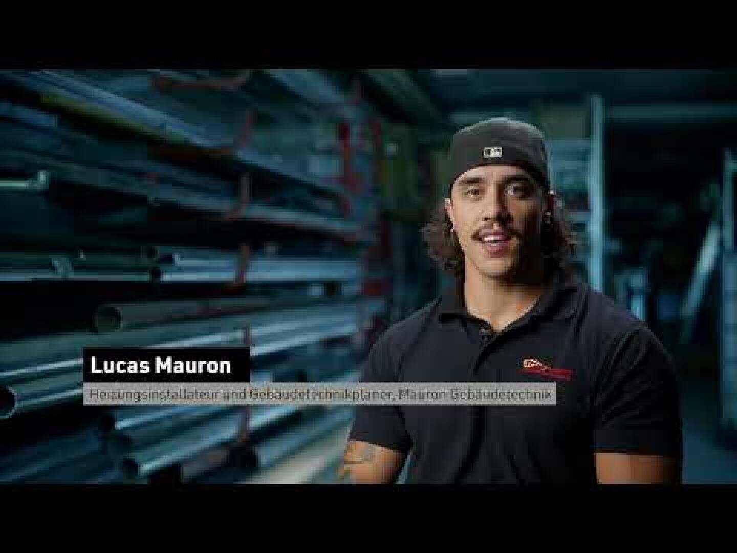 Ein Mann mit langen Haaren und einer Mütze spricht in einer Werkstatt, hinter ihm stehen Regale mit Metallrohren. In einem Textfeld auf der linken Seite steht: „Lucas Mauron – Heizungsinstallateur und Gebäudetechnikplaner, Mauron Gebäudetechnik“.