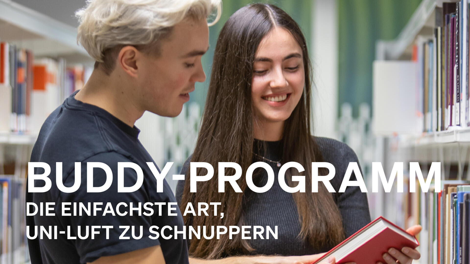 Zwei junge Erwachsene stehen in einem Bibliotheksgang, lächeln und schauen gemeinsam in ein aufgeschlagenes Buch. Der Text auf Deutsch lautet: Buddy-Programm: Die einfachste Art, Uni-Luft zu schnuppern.