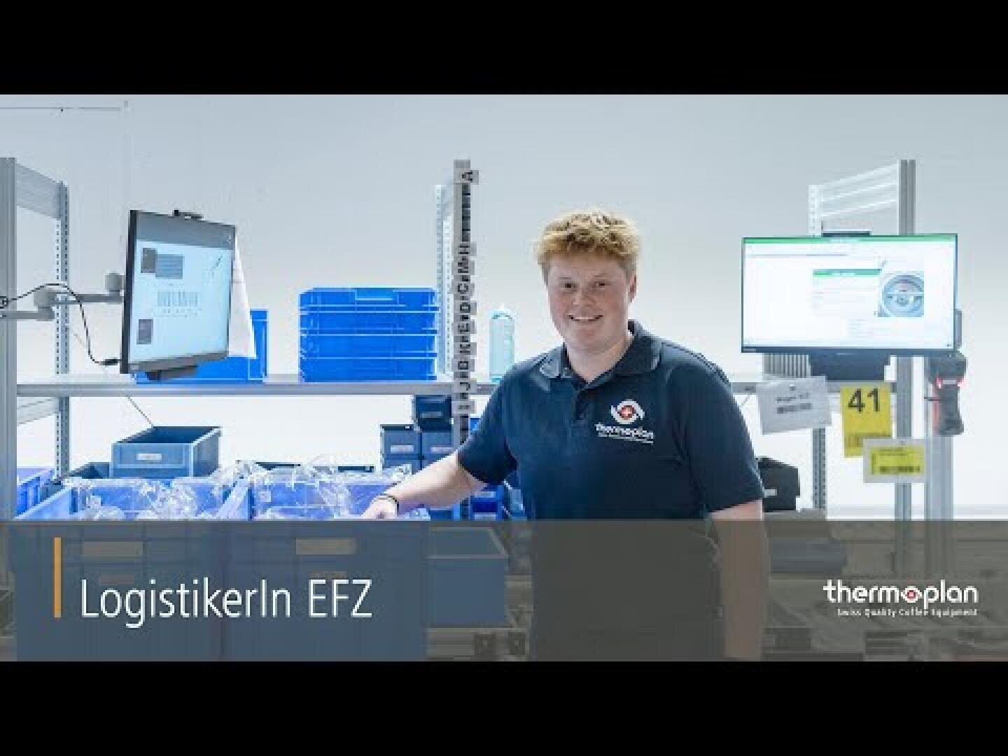 Eine Person mit kurzen Haaren steht lächelnd an einem Arbeitsplatz mit blauen Behältern, Computerbildschirmen und Geräten. Auf dem Bildschirm ist der Text „LogistikerIn EFZ“ und „thermoplan – Geräte in Schweizer Qualität“ zu lesen.